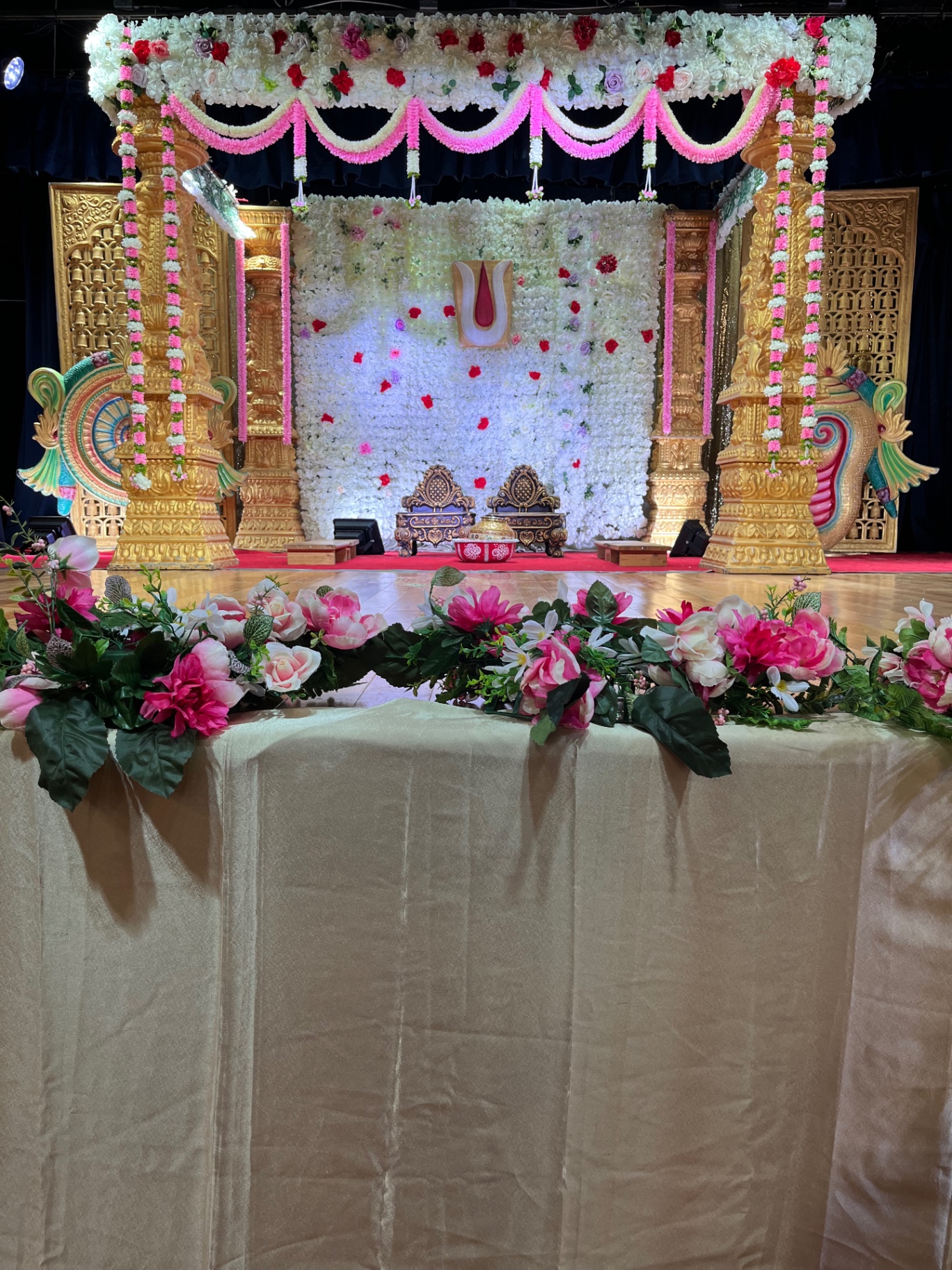 Pink and white floral mandap with gold pillars and peacock details