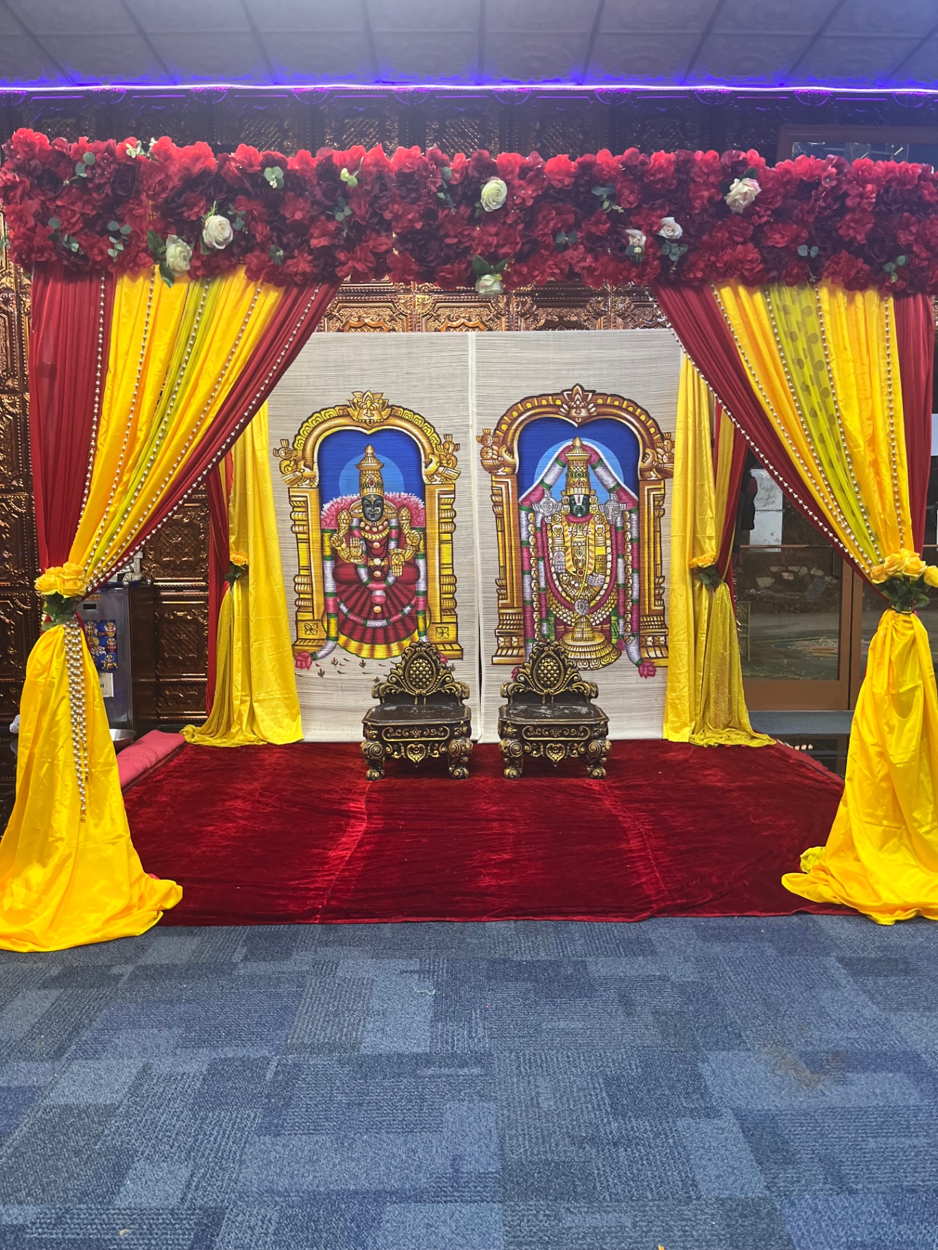 Traditional wedding stage with red and yellow draping and deity panels