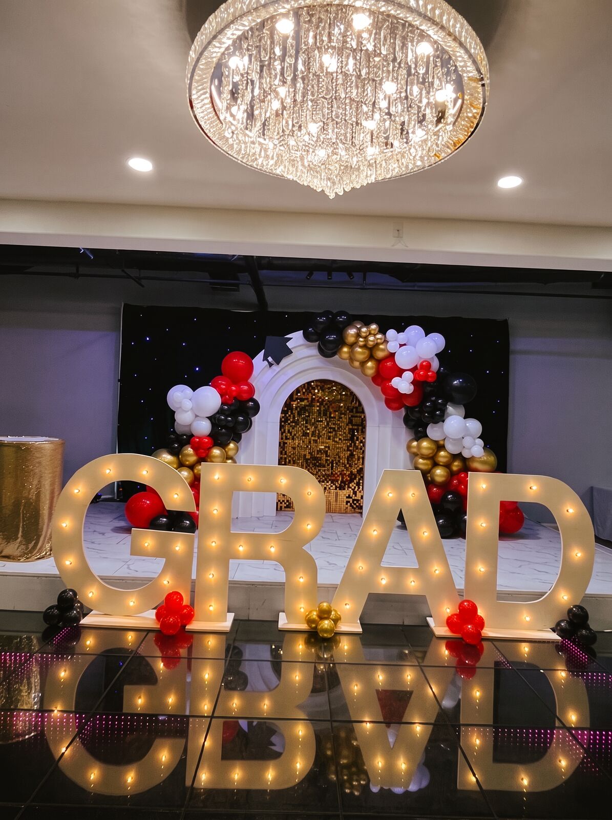 Graduation stage with a red, white and gold balloon arch