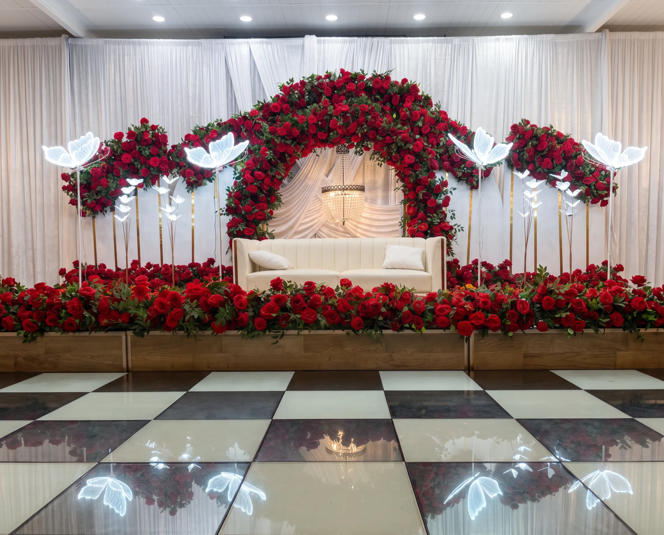 Red rose wedding reception stage with white draping, chandelier and illuminated butterfly details